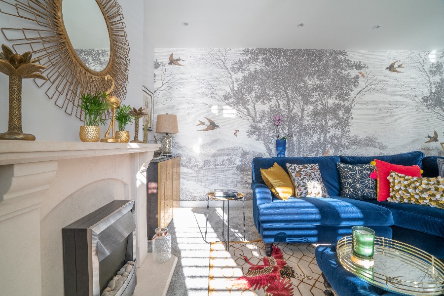Living room with floor-to-ceiling woodland and swallow mural wallpaper, cobalt blue velvet corner sofa, marble fireplace and gold sunburst mirror — residential interior design Princes Risborough Buckinghamshire