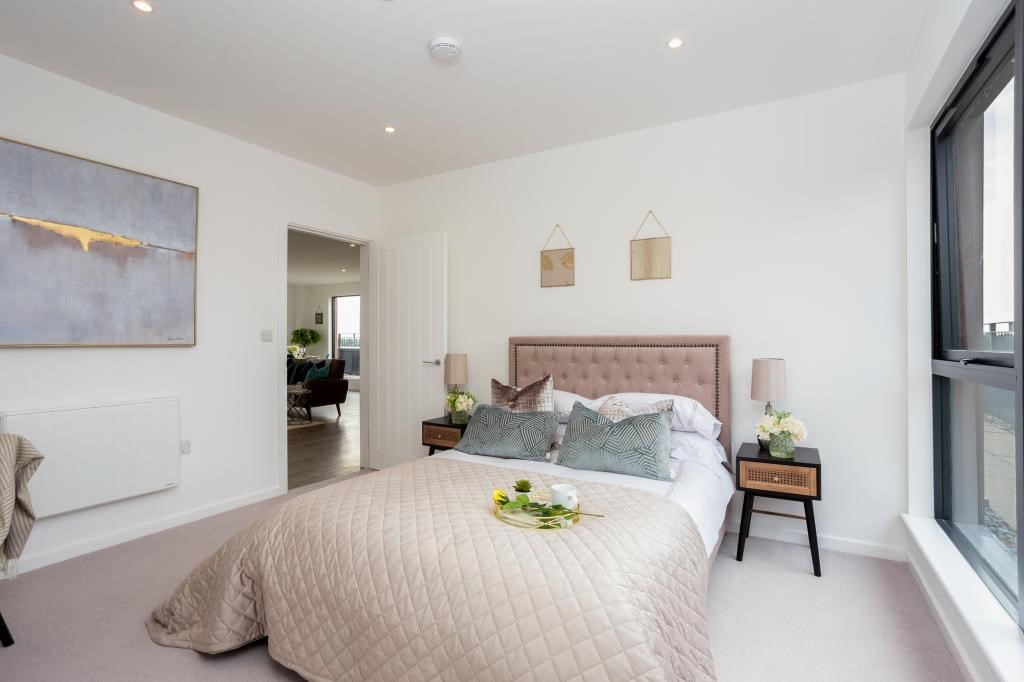 Penthouse second bedroom with blush pink buttoned headboard, sage green cushions, rattan bedside tables and large window — estate agent-developer interior styling Gerrards Cross