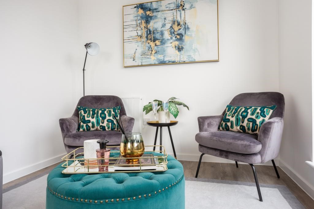 Penthouse living room seating area with teal buttoned ottoman, grey velvet armchairs, teal printed cushions and abstract gold artwork — property styling Gerrards Cross