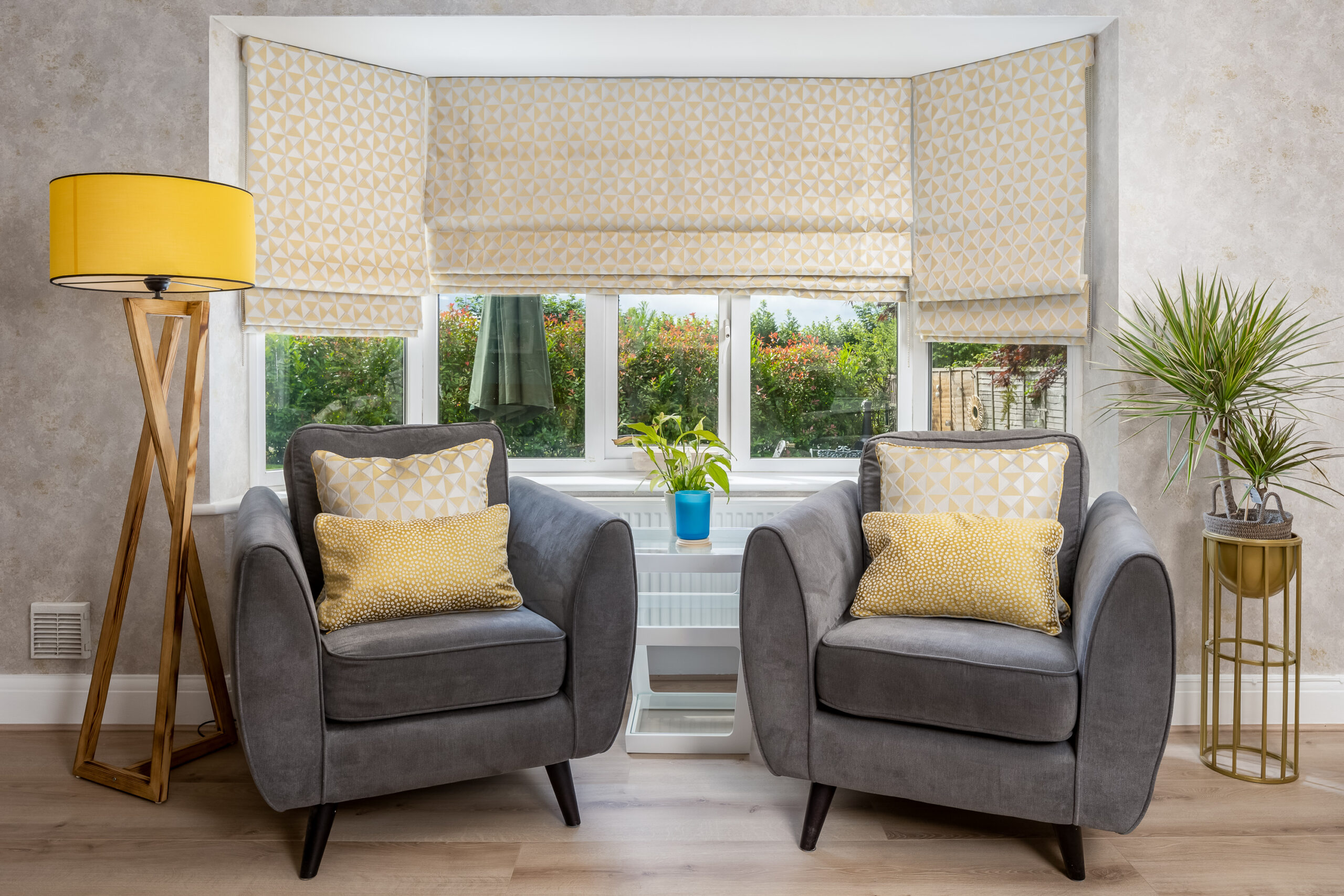 Bay window seating with pair of grey velvet armchairs, mustard geometric cushions, yellow floor lamp and lush garden views — biophilic family home interior design Penn Buckinghamshire
