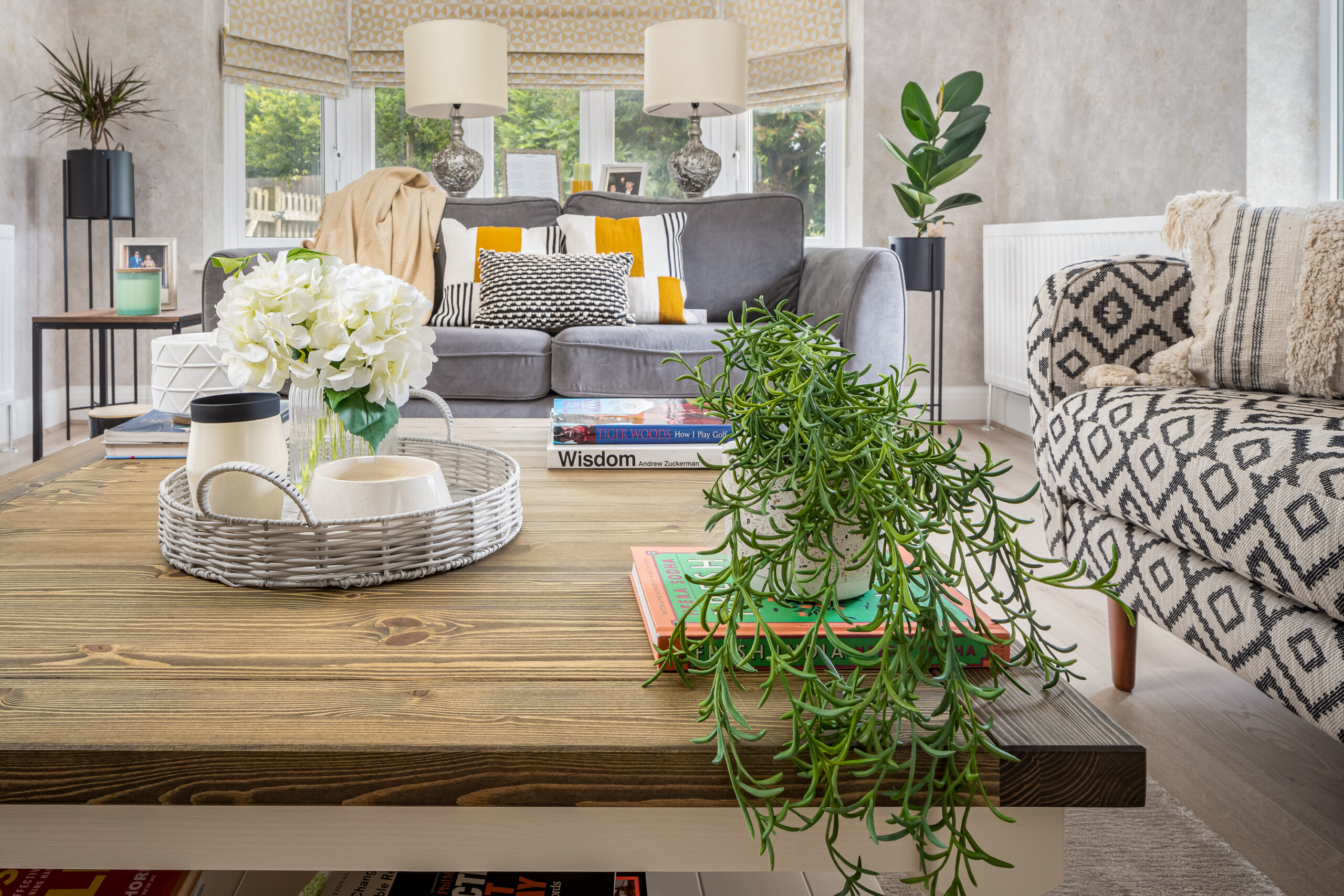 Styled living room coffee table with trailing succulent, wicker tray and white hydrangeas, grey sofa and garden views beyond. Family home interior design Penn Buckinghamshire