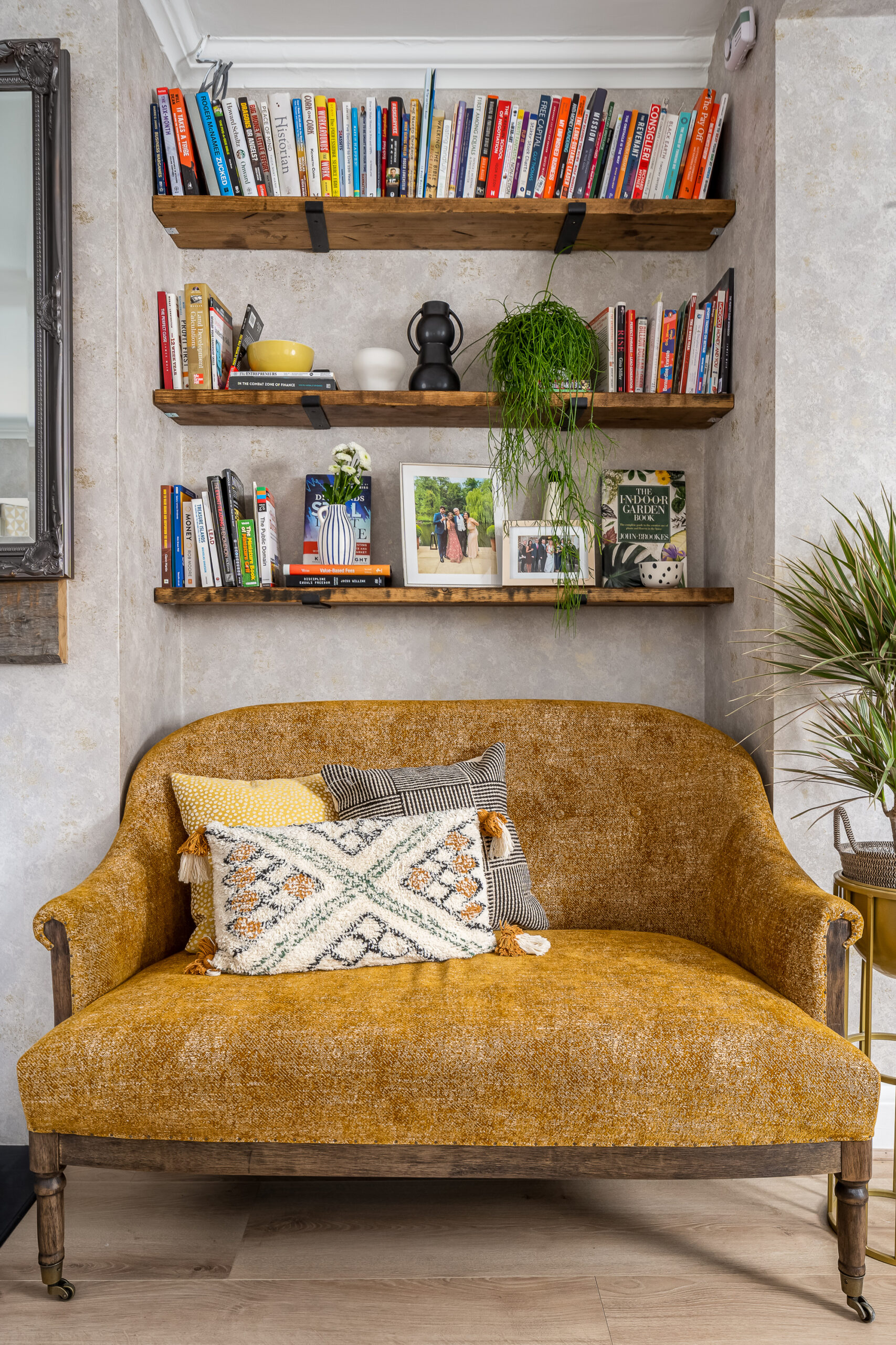 Mustard antique velvet sofa with reclaimed wood floating shelves, books, trailing houseplant and ceramic objects — family home interior design Penn Buckinghamshire