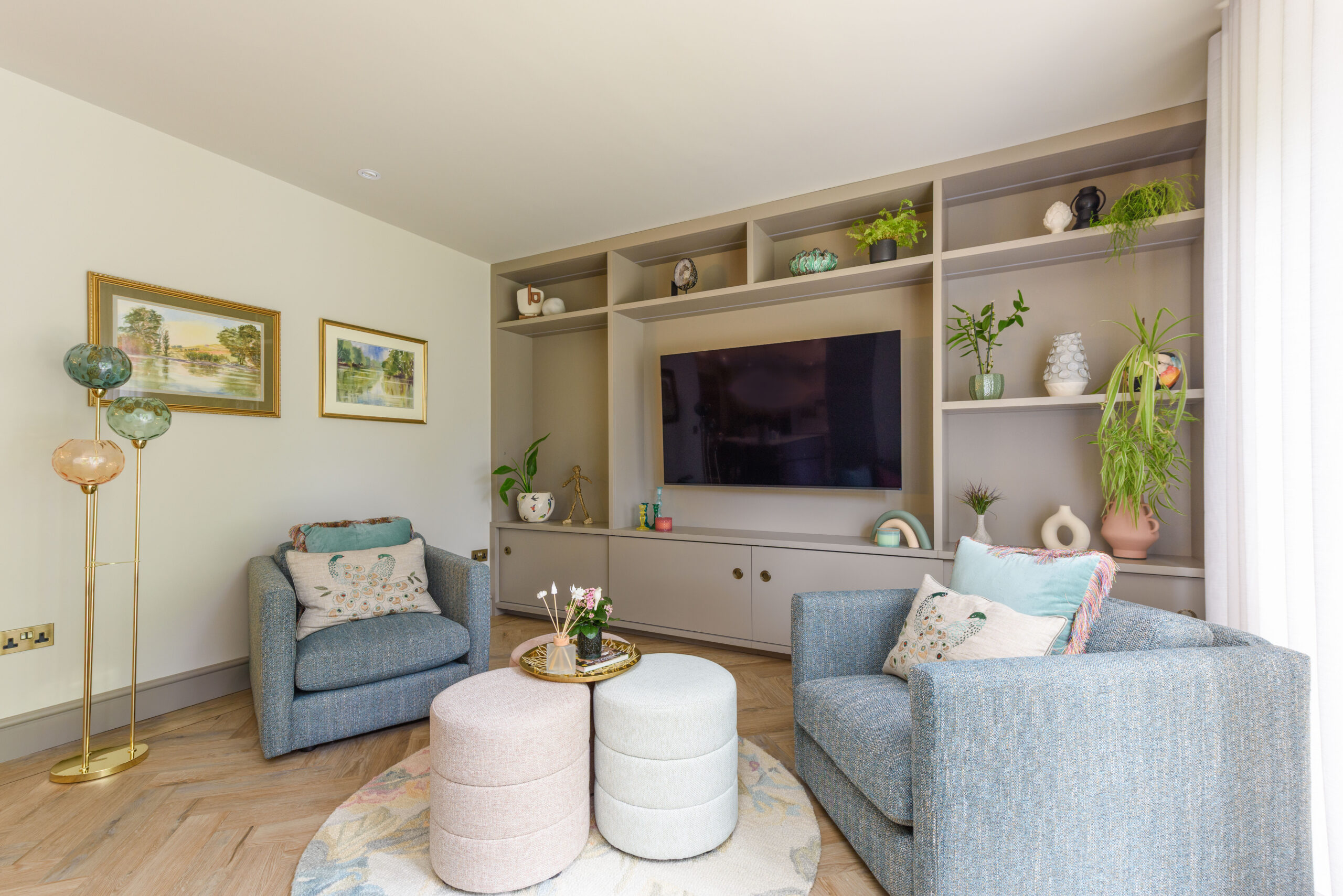 Bespoke fitted shelving unit with integrated TV, houseplants and ceramics, blue-grey armchairs and brass floor lamp — family living room interior design Buckinghamshire