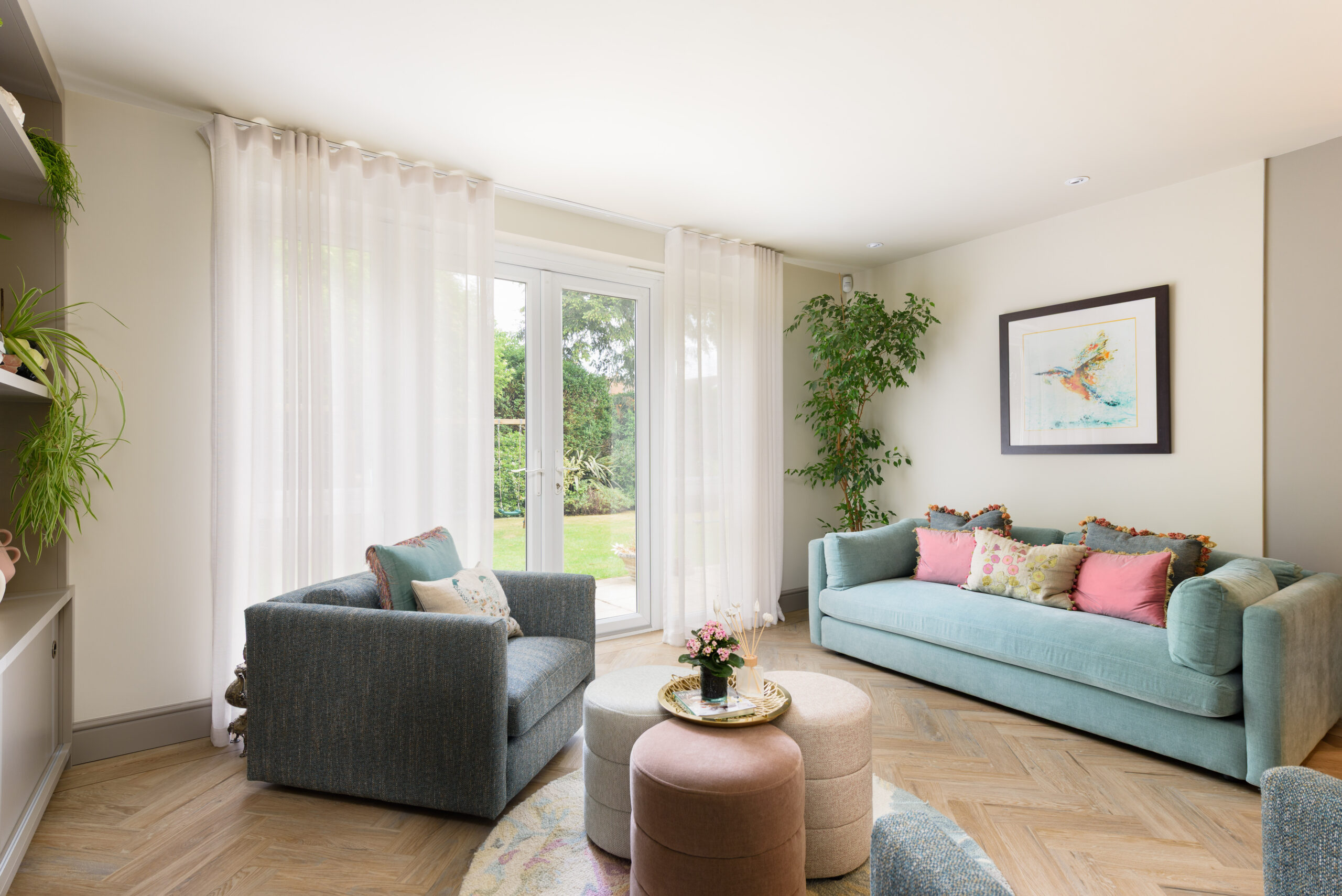 Light-filled family living room with duck egg blue sofa, sheer linen curtains, tall indoor tree and garden views through French doors — biophilic interior design Buckinghamshire