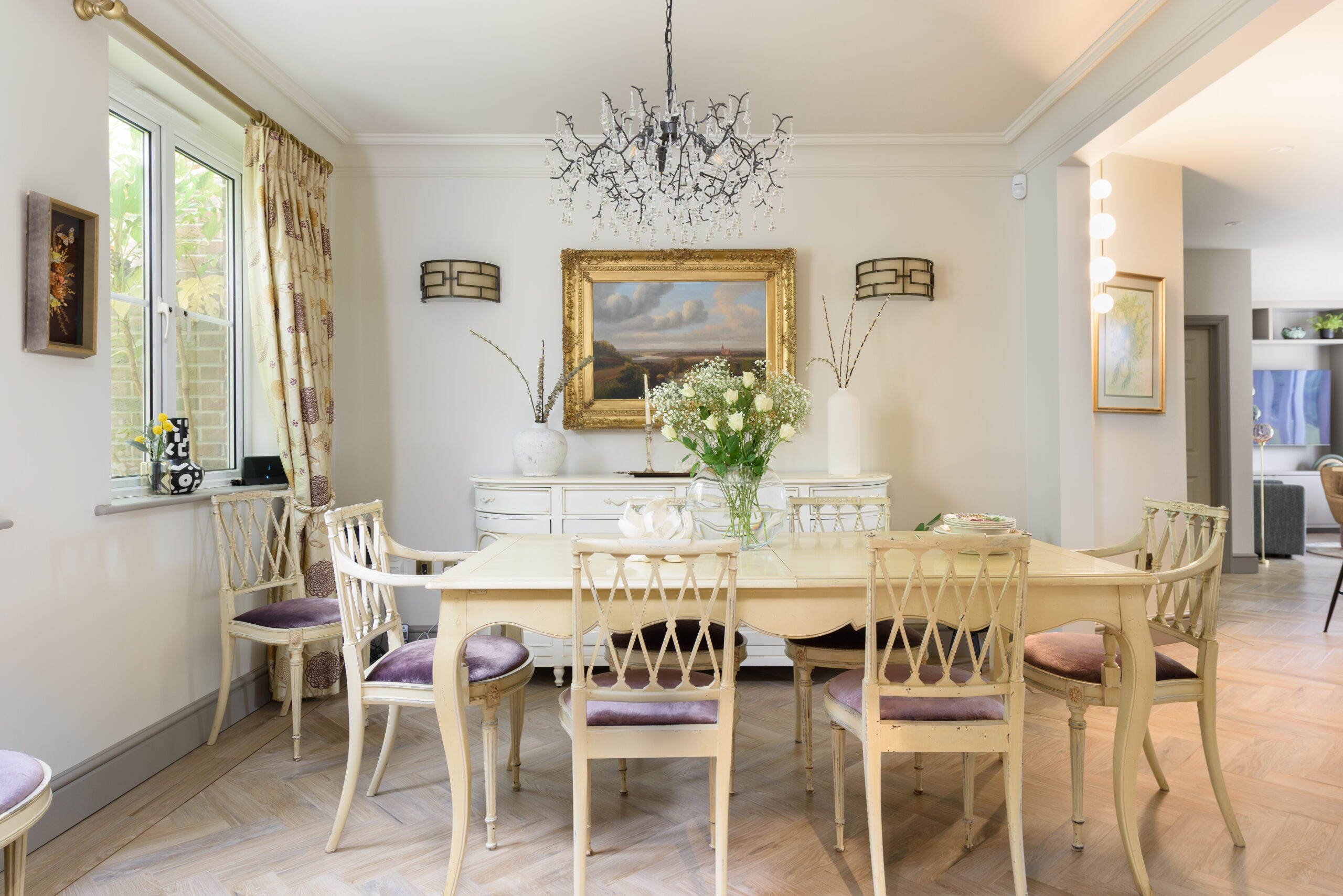 Elegant dining room with antique French cream chairs, crystal branch chandelier, gold-framed oil painting and herringbone oak floor — residential interior design Buckinghamshire