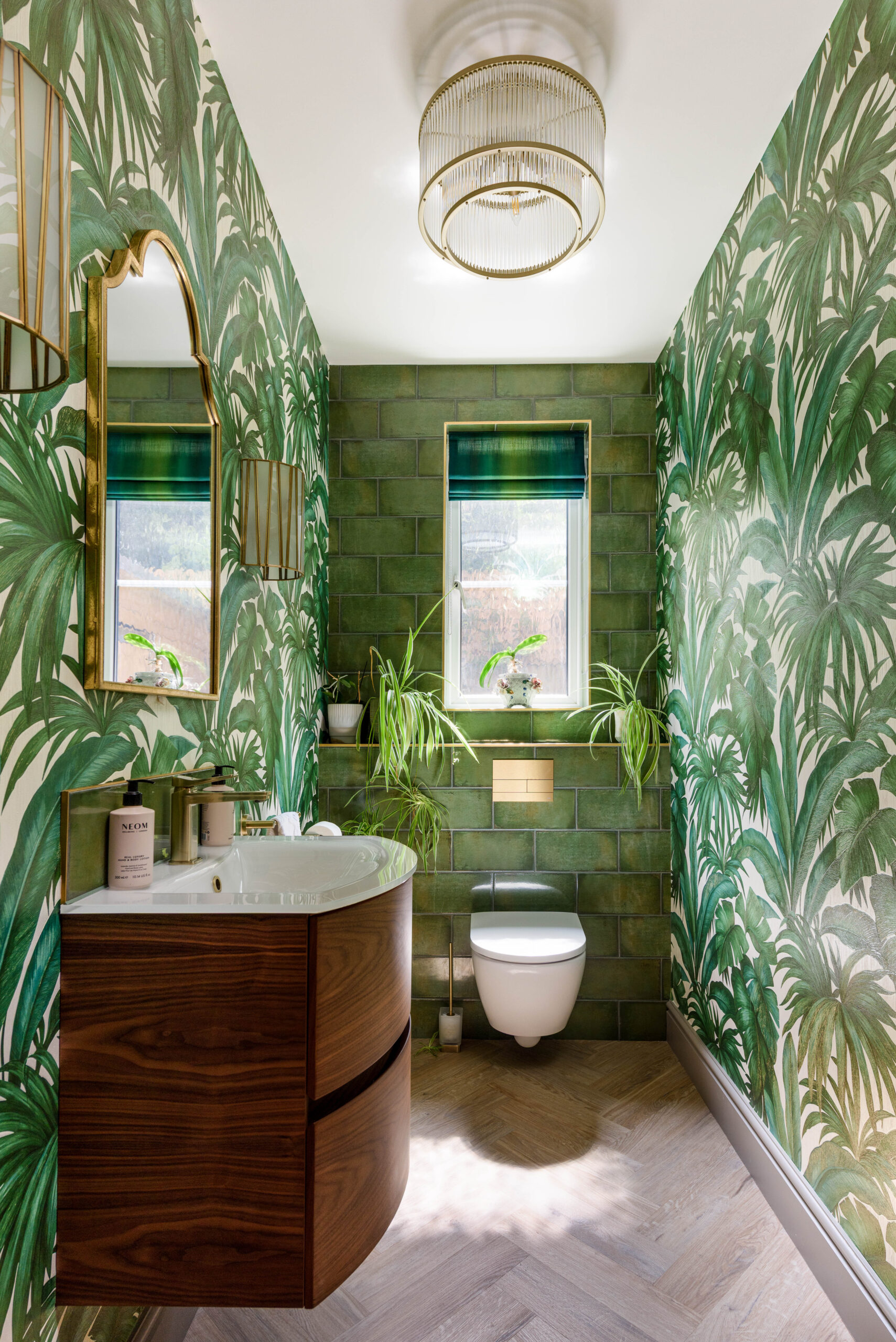 Biophilic guest cloakroom with tropical leaf wallpaper, green glazed tiles, walnut vanity unit and herringbone floor — residential interior design Buckinghamshire